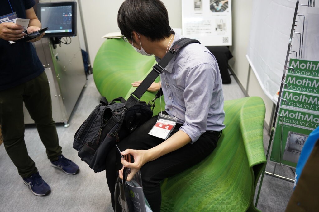 エス.ラボ社のブース内にある、樹脂で造形された3人掛けベンチとそこに座る人